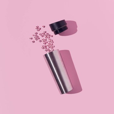 Yumuşak pembe arka planda küçük kırmızı kalpleri olan gümüş termos. En az Sevgililer Günü konsepti.