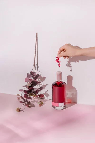 Mano Femenina Botella Bebida Alcohólica Con Frutas Rojas Sobre Fondo — Foto de Stock