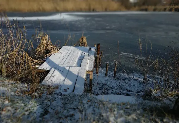 Donmuş bir gölün kıyısında karla kaplı bir köprü..