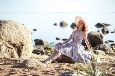 Büyük hasır şapkalı güzel bir kız vahşi deniz kıyısında dinleniyor..