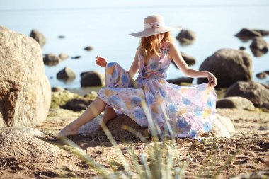 Büyük hasır şapkalı güzel bir kız vahşi deniz kıyısında dinleniyor..