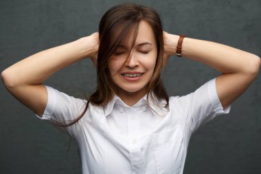 Katı giysili, gülümseyen bir kızın portresi ellerini gri duvara dayayıp duruyor..