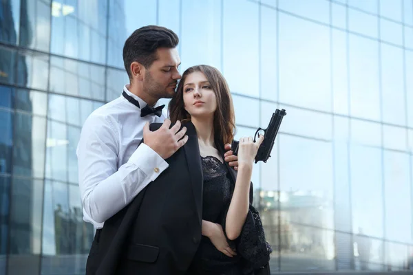 Zarif, zarif bir adam elinde silah olan güzel bir kıza sarılıyor..