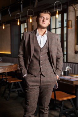 Lokantanın iç tarafındaki bar tezgahının yanında şık takım elbiseli şık genç adam..