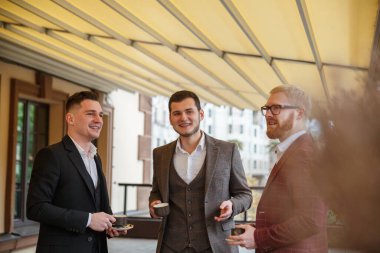 Takım elbiseli üç adam terasta bir fincan kahve için konuşuyor..