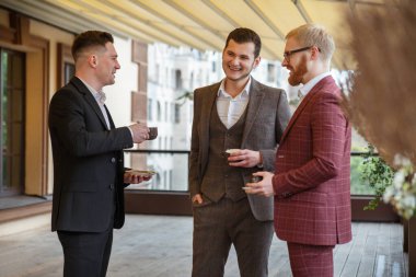 Takım elbiseli üç adam terasta bir fincan kahve için konuşuyor..