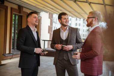 Takım elbiseli üç adam terasta bir fincan kahve için konuşuyor..