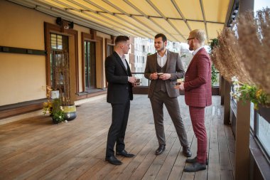 Takım elbiseli üç adam terasta bir fincan kahve için konuşuyor..