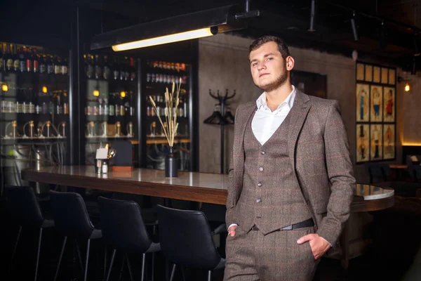 Stylish young man in elegant three-piece suit near bar counter in restaurant interior.