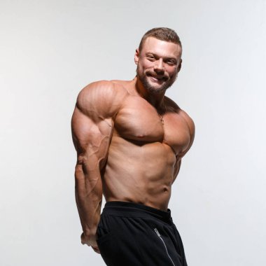 Genç kaslı vücut geliştiren adam, açık gri arka planda izole edilmiş kaslarını gösteriyor..