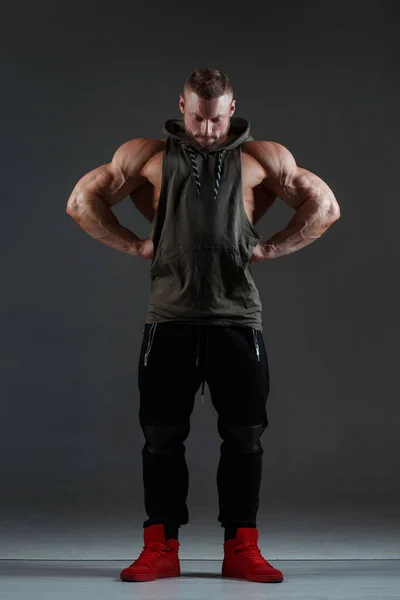 運動白人男性は暗い背景の下で完全な成長に立って筋肉を示しています — ストック写真