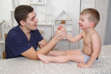 Doktor masaj terapisti evde gülümseyen bir çocuğa el masajı yapıyor..