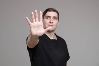 Gündelik çalışan siyah elbiseli genç beyaz adam avucu gri bir arka planda izole edilmiş bir şekilde yolunu kapatıyor, eline odaklan..