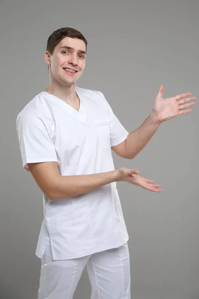 穿着医疗工作服的年轻人指着某样东西 他的手被灰色背景隔开了 — 图库照片