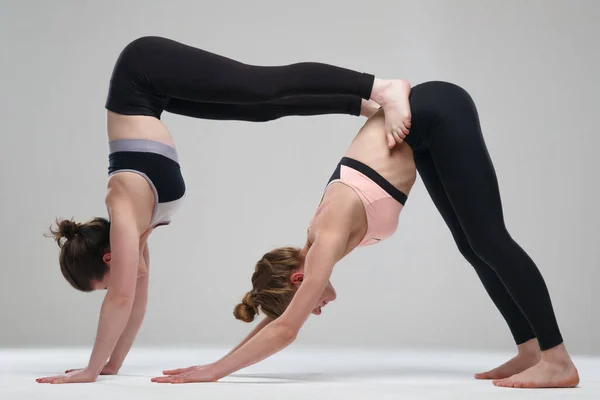 两个女孩在灰色背景下练习瑜伽 — 图库照片