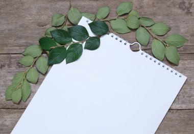 Kayıt için bir defterden alınmış beyaz bir sayfa yaprak ve dallardan oluşan eski bir ahşap masa üzerinde yatar..