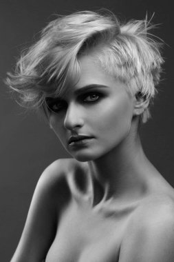 Gri bir arka planda kısa saç kesimi olan tatlı, küllü sarışın bir kızın siyah beyaz portresi..