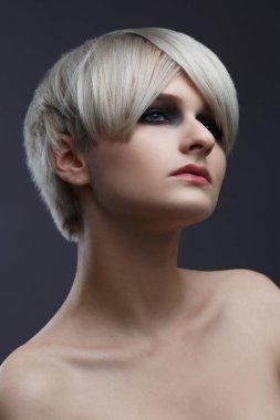Gri bir arka planda kısa saç kesimi olan tatlı, küllü sarışın bir kızın güzel portresi..