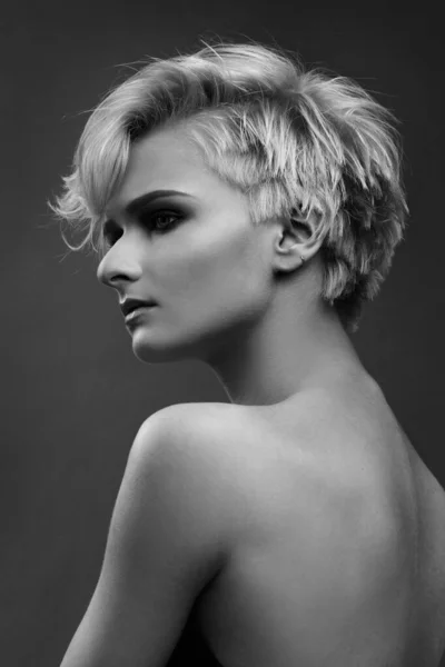 Black and white beauty portrait of a cute ash blonde girl with a short stylish haircut on a gray background.