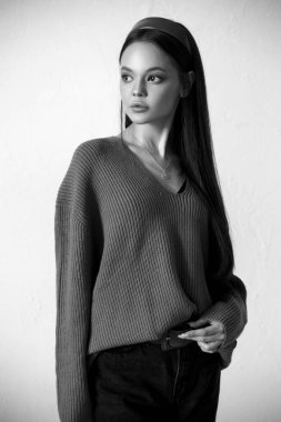 Gri arka planda rahat bir süveter giyen siyah beyaz bir kızın portresi..