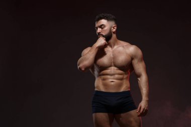 Koyu gri arka planda izole olmuş kaslarını gösteren çıplak gövdeli genç bir sporcunun portresi..