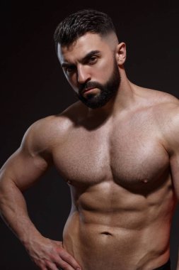 Sakallı genç atletik erkek sporcu koyu bir arka planda izole olmuş kaslar gösteriyor..
