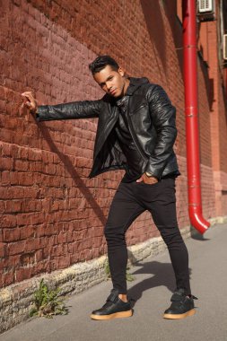 Sokakta kırmızı tuğlalı duvarın yanında siyah deri ceketli yakışıklı dansçı..