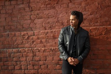 Siyah deri ceketli yakışıklı adam, dışarıdaki kırmızı tuğladan duvara yaslanıyor..