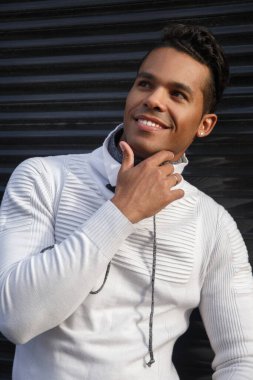 Yüzünde bir gülümseme olan, dışarıda siyah bir arka planda şık beyaz günlük kıyafetler giyen, mutlu, çekici bir Latin adamın portresi..