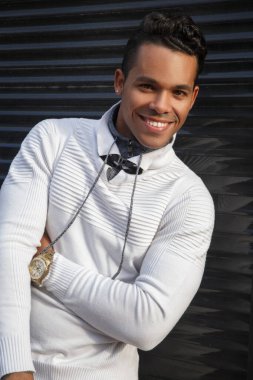 Yüzünde bir gülümseme olan, dışarıda siyah bir arka planda şık beyaz günlük kıyafetler giyen, mutlu, çekici bir Latin adamın portresi..