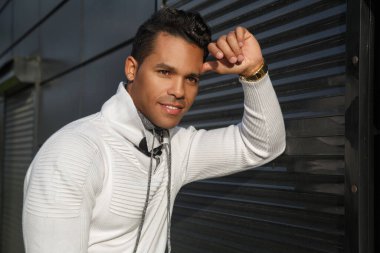 Yüzünde bir gülümseme olan, dışarıda siyah bir arka planda şık beyaz günlük kıyafetler giyen, mutlu, çekici bir Latin adamın portresi..