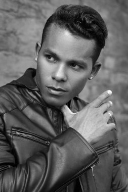 Siyah beyaz bir portre, siyah deri ceketli yakışıklı bir Latin 'in tuğla bir duvarın arkasında duran portresi..