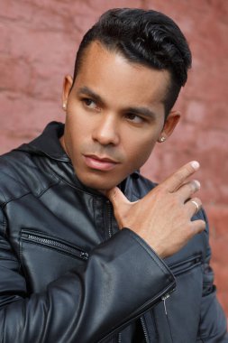 Siyah deri ceketli yakışıklı bir Latin 'in portresi kırmızı tuğlalı bir duvarın arkasında..