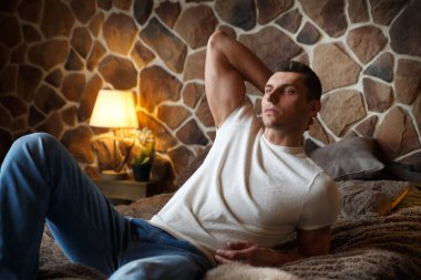 Genç ve yakışıklı bir adam rahat bir şekilde dinleniyor. Yatak odasında, kırsal bir iç mekanı olan bir yatakta..