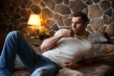 Genç ve yakışıklı bir adam rahat bir şekilde dinleniyor. Yatak odasında, kırsal bir iç mekanı olan bir yatakta..