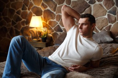 Genç ve yakışıklı bir adam rahat bir şekilde dinleniyor. Yatak odasında, kırsal bir iç mekanı olan bir yatakta..