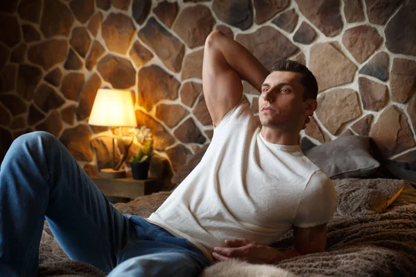 Genç ve yakışıklı bir adam rahat bir şekilde dinleniyor. Yatak odasında, kırsal bir iç mekanı olan bir yatakta..