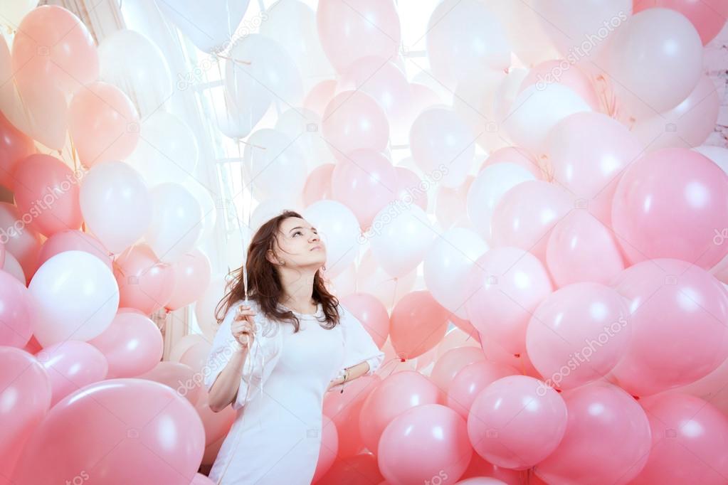 Girl in white flies among pink balloons