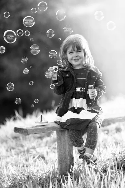 Black-and-white portrait of a girl sitting on a wooden bench blo — Stock Photo, Image