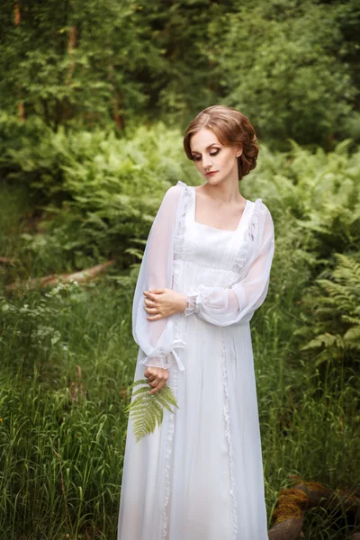 Fille sur le bord de la forêt dans une longue robe blanche avec une fougère dans les mains de — Photo