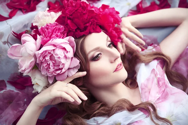 Woman in a wreath of peonies lies among petals — Stock Photo, Image