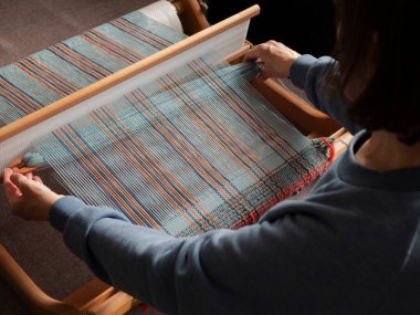 El dokumacı çalışıyor. Dokuma tezgahı kullanarak çizgili kumaş yapmak