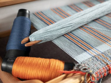 Handloom with shuttle on the blue warp threads and two bobbins with indigo and orange yarns. Vertical stripe weave clipart