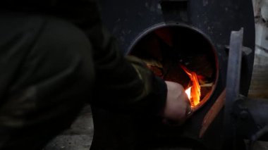 Kişi odun sobasındaki odunları yakıyor. Karanlıktaki ateşin alevi