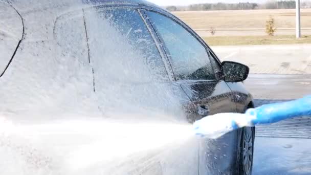 自動洗車でスプレーワンドで自動車に石鹸を適用します サッドで車全体をスプレーするために男は車の周りにラップを取っています — ストック動画