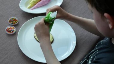 Çocuk şekerli kurabiyeleri krema ve renkli şekerlerle süslüyor. Çocuk, yenilebilir süslemelerle eğlenceli ve güzel kurabiye tasarımı yapıyor.