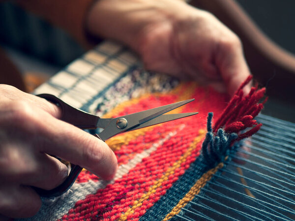 Master weaver is cutting the ends of the threads to create a cut pile carpet effect. Making coloured tapestry, close up