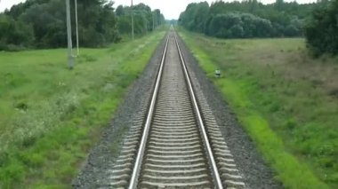 Tren raylarda ilerliyor ve otlakları, köyü, köprüyü geçiyor. Son tren vagonundan görüntü
