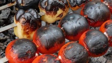 Domates ve dolma biber kızgın kömürlerin üstünde kızarıyor. Kızarmış sebzeleri hazırlayın. Şişte renkli sebzeler