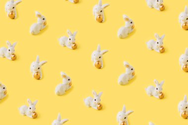 Tavşanlardan yapılmış bir kalıp, sarı arka plana karşı Paskalya konsepti. Tavşan altın bir Paskalya yumurtası tutuyor. En düşük düzlük.